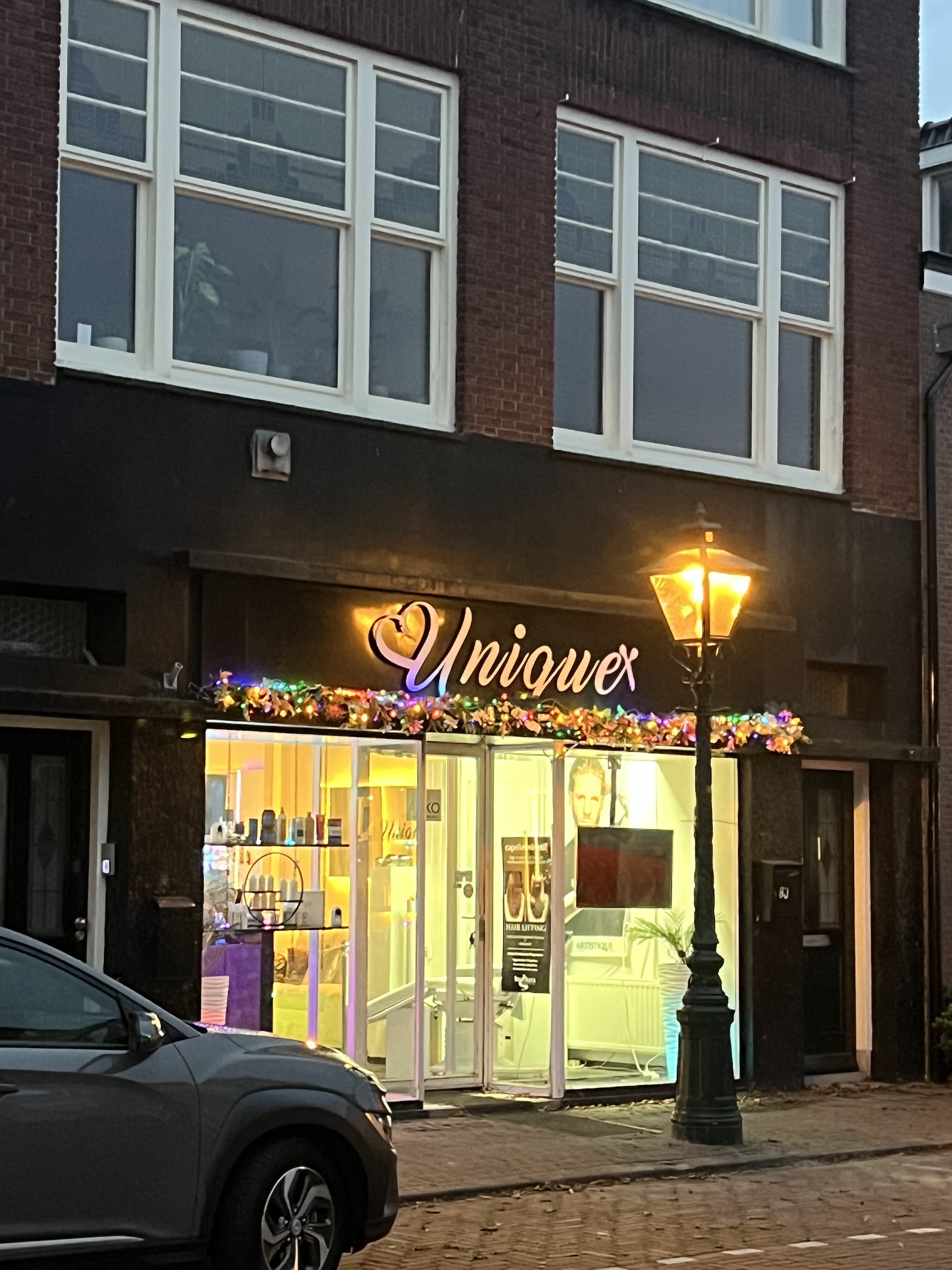 De salon Unique aan de Herenstraat bij avond, met de verlichte gevelletters en een straatlantaarn